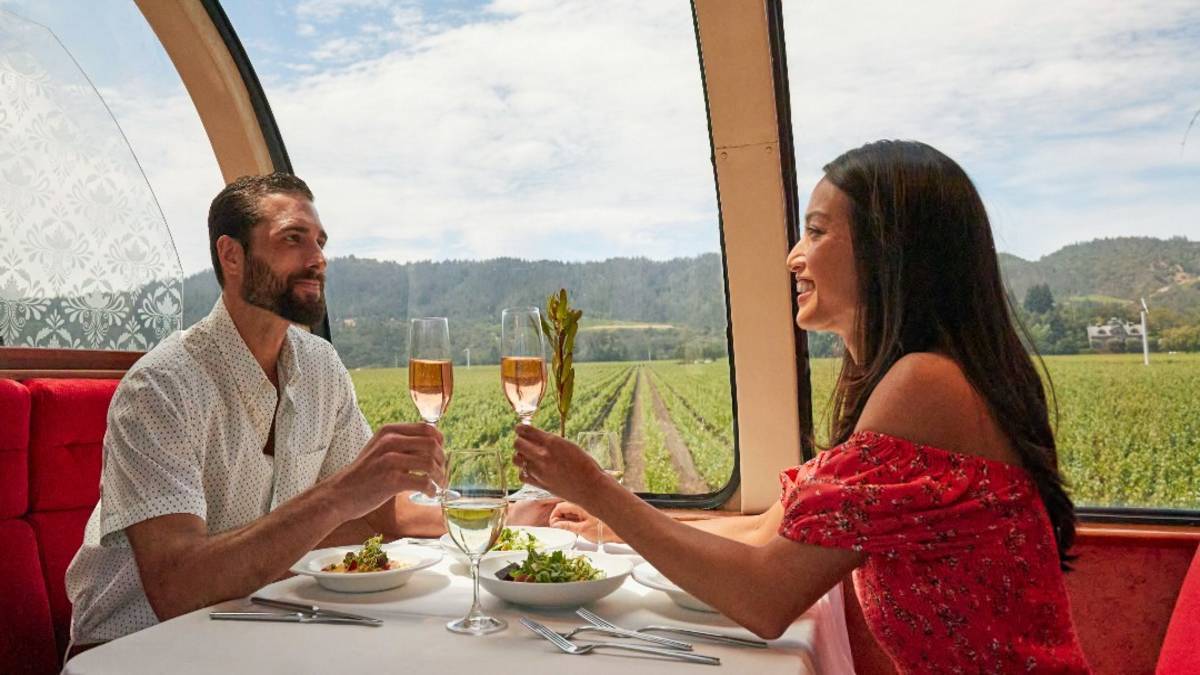 A couple at a dinner table set with two plates and a white table cloth with champagne glasses in their hands